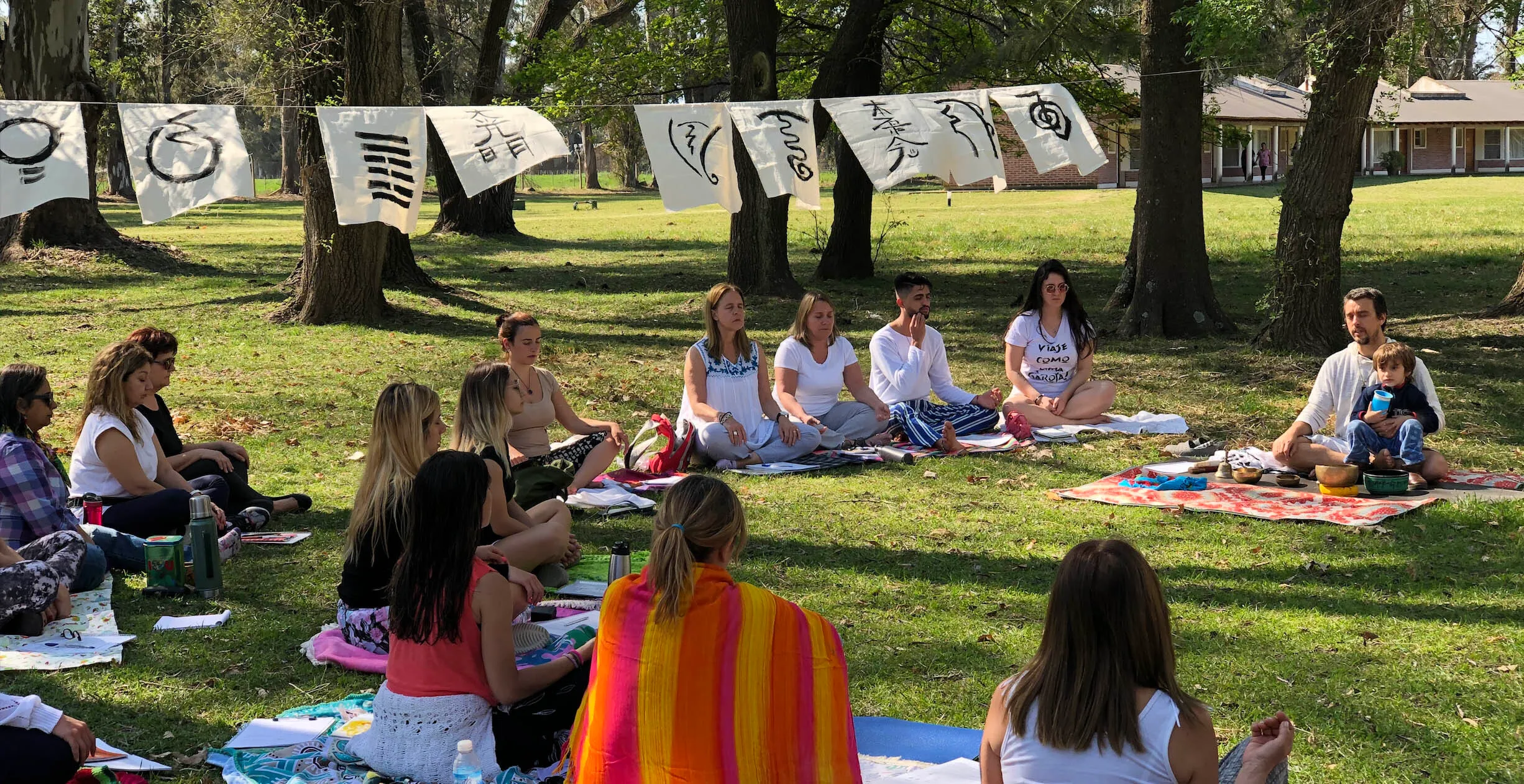 Mati Mahia con un grupo de practicantes en círculo durante un retiro al aire libre, con kanji colgados entre los árboles